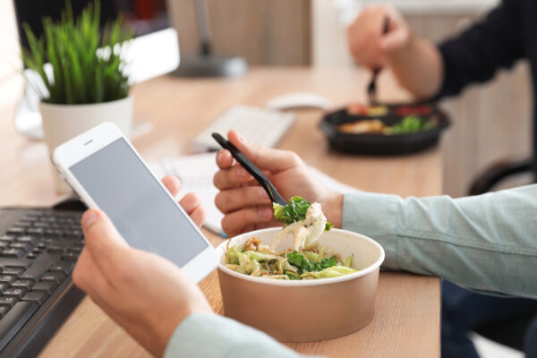 An office worker holds a cell phone while working through their lunch.